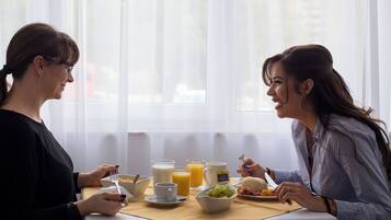 Deux personnes sont assises à une table où sont servis des aliments pour le petit-déjeuner, notamment des céréales, du lait, du jus de fruits et des fruits.