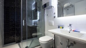 Un baño moderno con ducha de vidrio, inodoro blanco y lavamanos con espejo arriba.