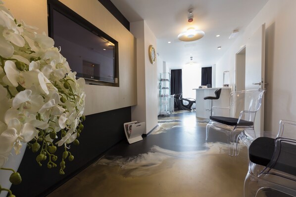 Ein modernes Interieur mit einem Flur, der in einen Salonbereich führt, mit einem großen Spiegel, klaren Stühlen und einer dekorativen Orchideenkomposition.