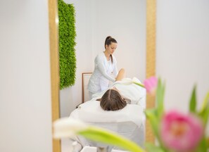 Ein Spa-Raum mit Massagetisch, einer Person, die eine Massage erhält, und einer an der Wand befestigten Zimmerpflanze.