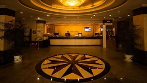 Een hotel lobby met een centraal receptiegedeelte, een kroonluchter en een decoratief vloerpatroon.