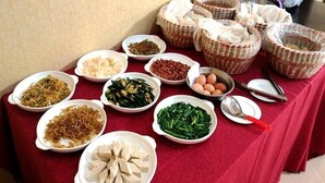Een tafel met verschillende soorten eten en bestek, waaronder schalen met groenten, tofu en eieren, evenals manden en een lepel.