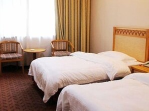 A hotel room with two beds, a small round table, two chairs, and a window with curtains.