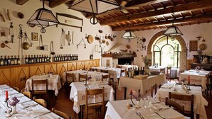 A restaurant with multiple tables set for dining, a wine rack on the wall, and a fireplace. - Al Vecchio Convento (Portico e San Benedetto)