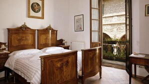 A bedroom with a wooden bed, a nightstand, a framed picture on the wall, and a window with a view of a stone building. - Al Vecchio Convento (Portico e San Benedetto)