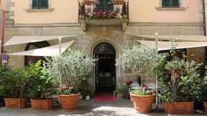 A building with a central entrance, potted plants, outdoor umbrellas, and a balcony with flowers. - Al Vecchio Convento (Portico e San Benedetto)