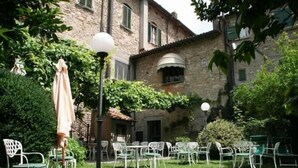 A courtyard with outdoor seating, a lamp post, and a stone building in the background. - Al Vecchio Convento (Portico e San Benedetto)