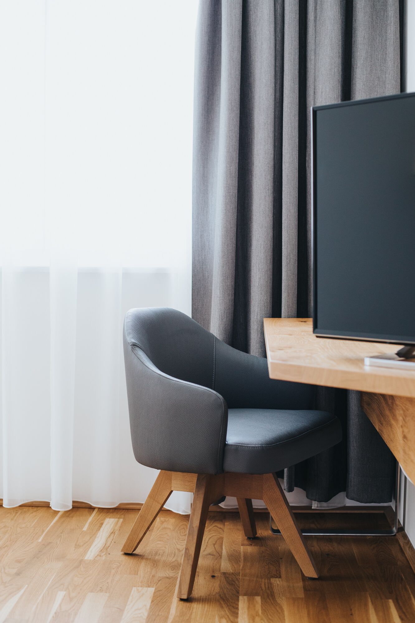 Una habitación moderna con un escritorio de madera, una silla tapizada de gris y un monitor negro grande.