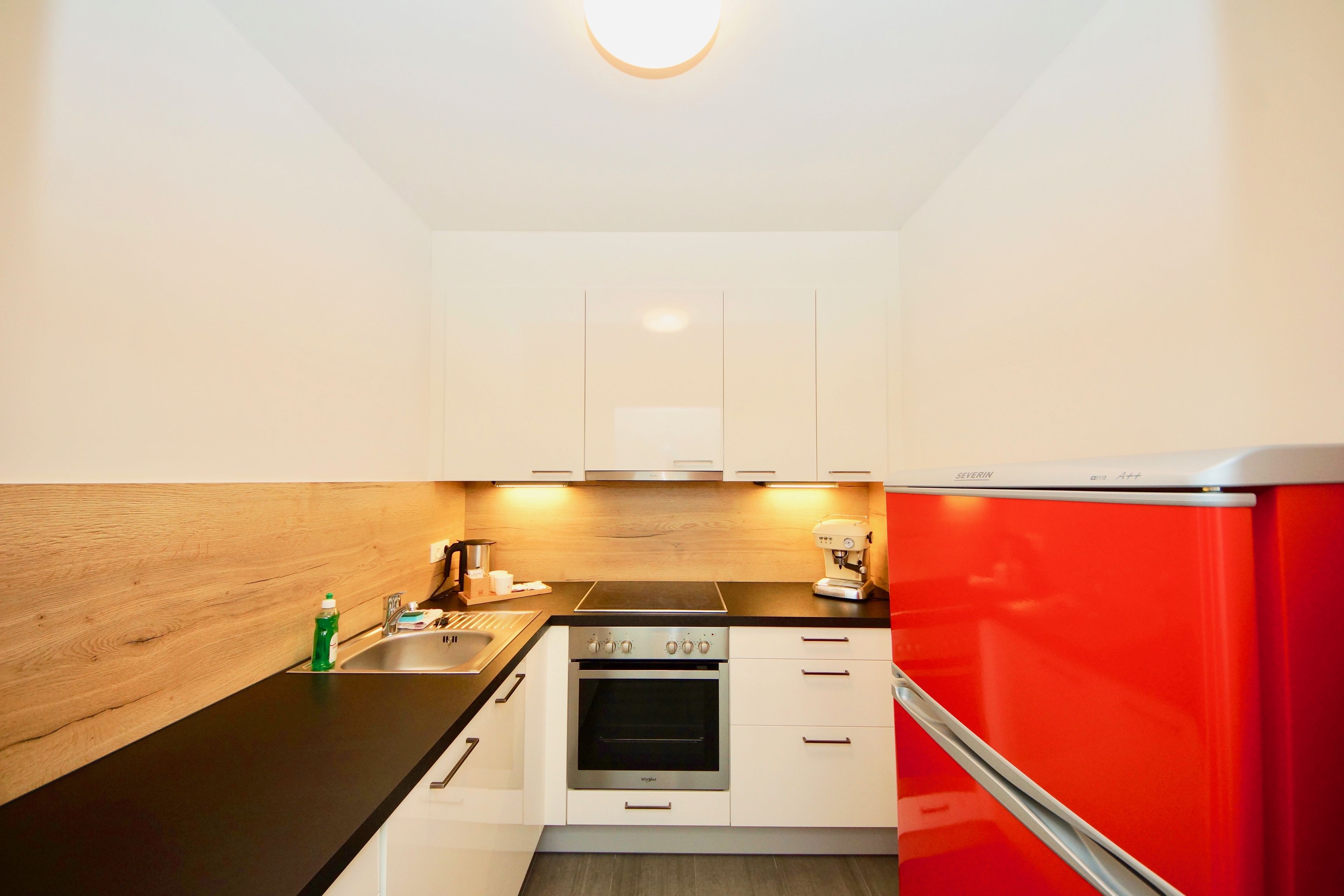 A modern kitchen with white cabinets, a black countertop, and a red refrigerator.