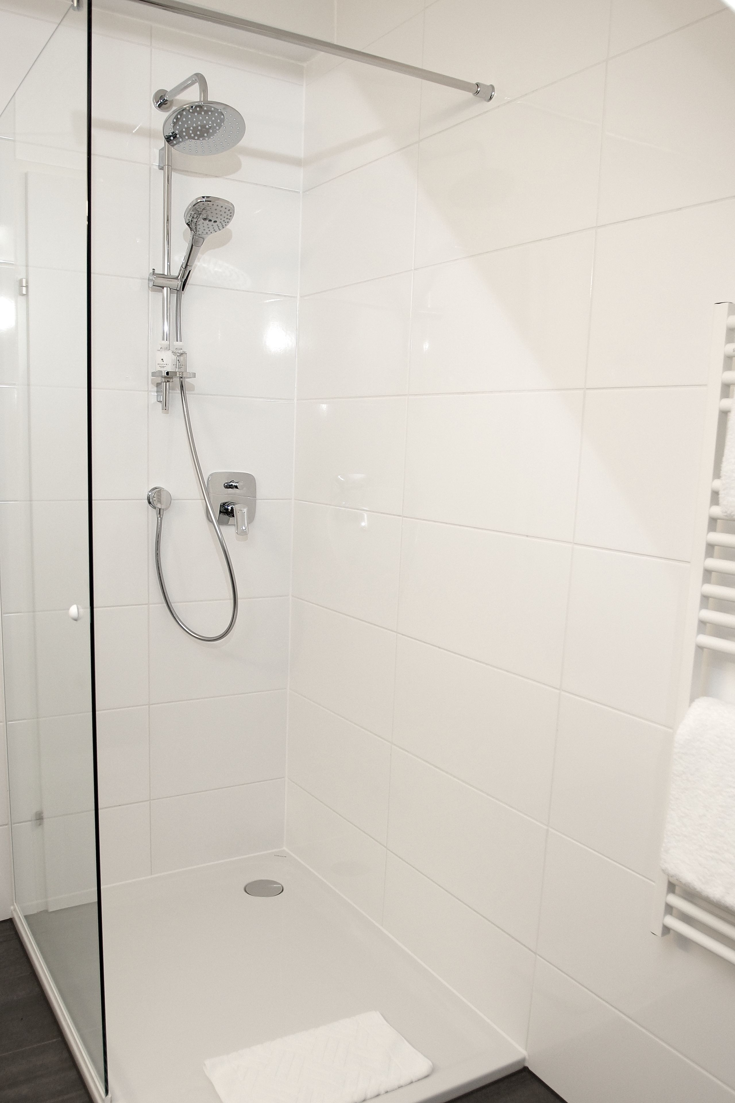 A glass-enclosed shower with a handheld showerhead and a wall-mounted faucet.