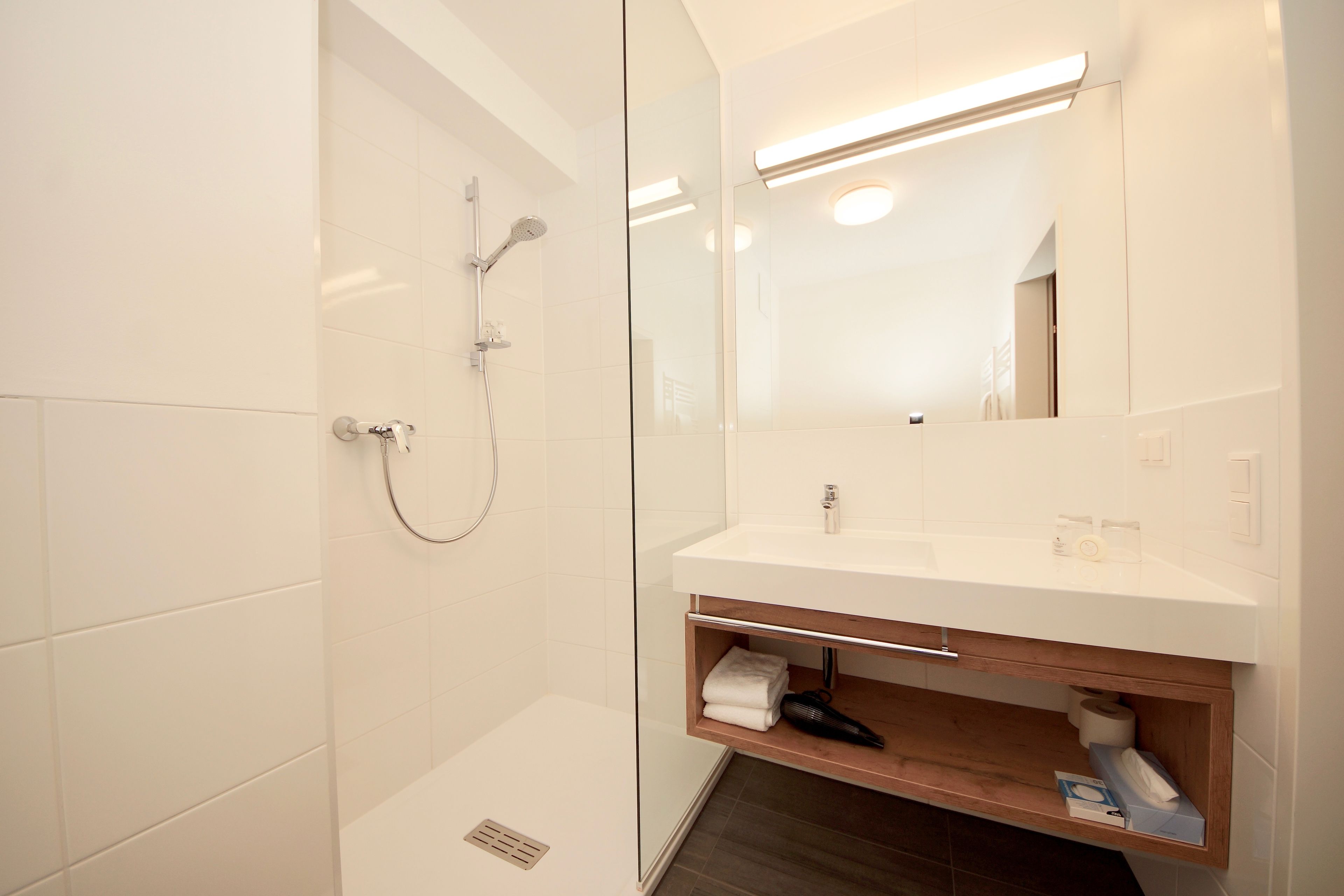 A modern bathroom with a glass-enclosed shower, a white sink with a wooden shelf, and a mirror above the sink.
