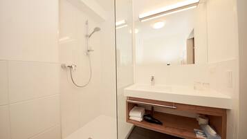 A modern bathroom with a glass-enclosed shower, a white sink with a wooden shelf, and a mirror above the sink.