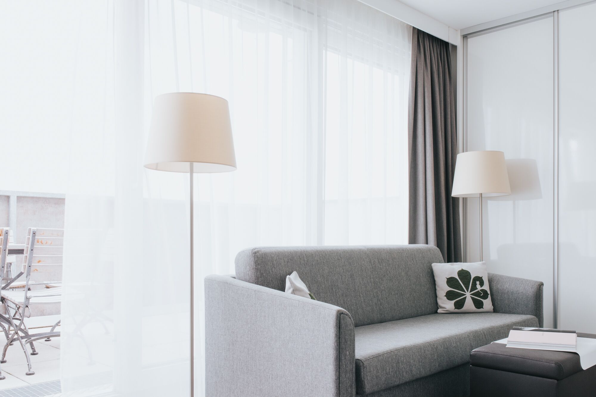 Una habitación de hotel moderna con un sofá gris, una mesita y dos lámparas de pie.