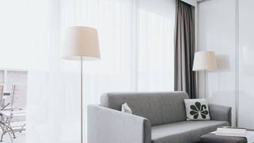 Una habitación de hotel moderna con un sofá gris, una mesita y dos lámparas de pie.