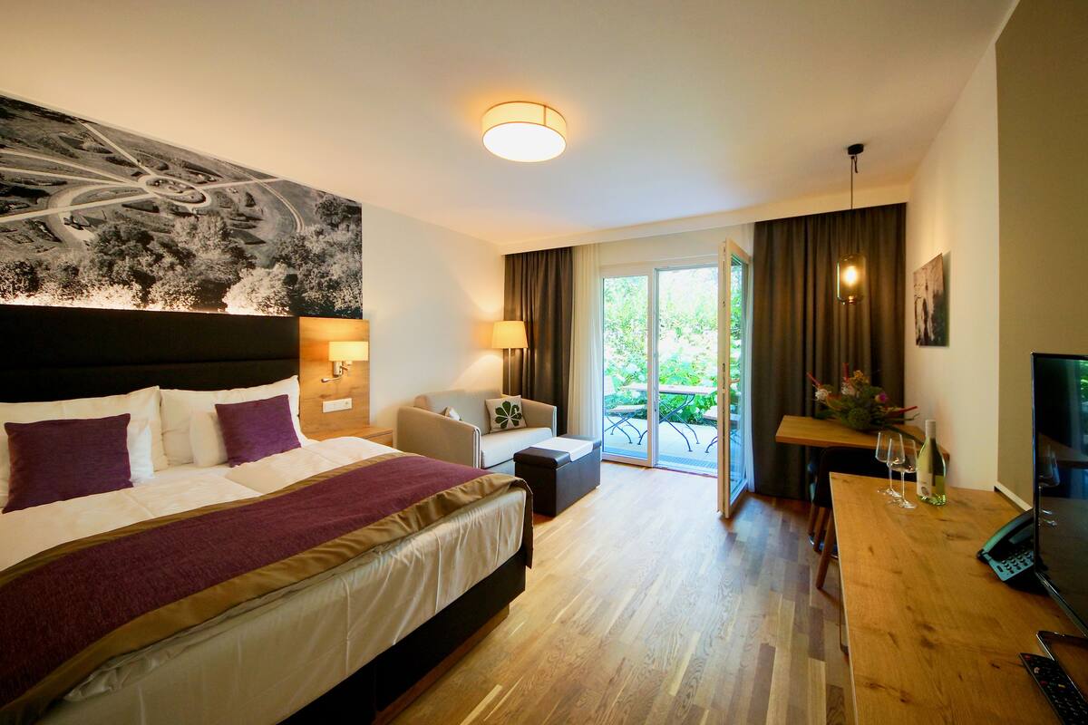 Quarto de hotel com uma cama grande, escrivaninha, cadeira e varanda com vista.