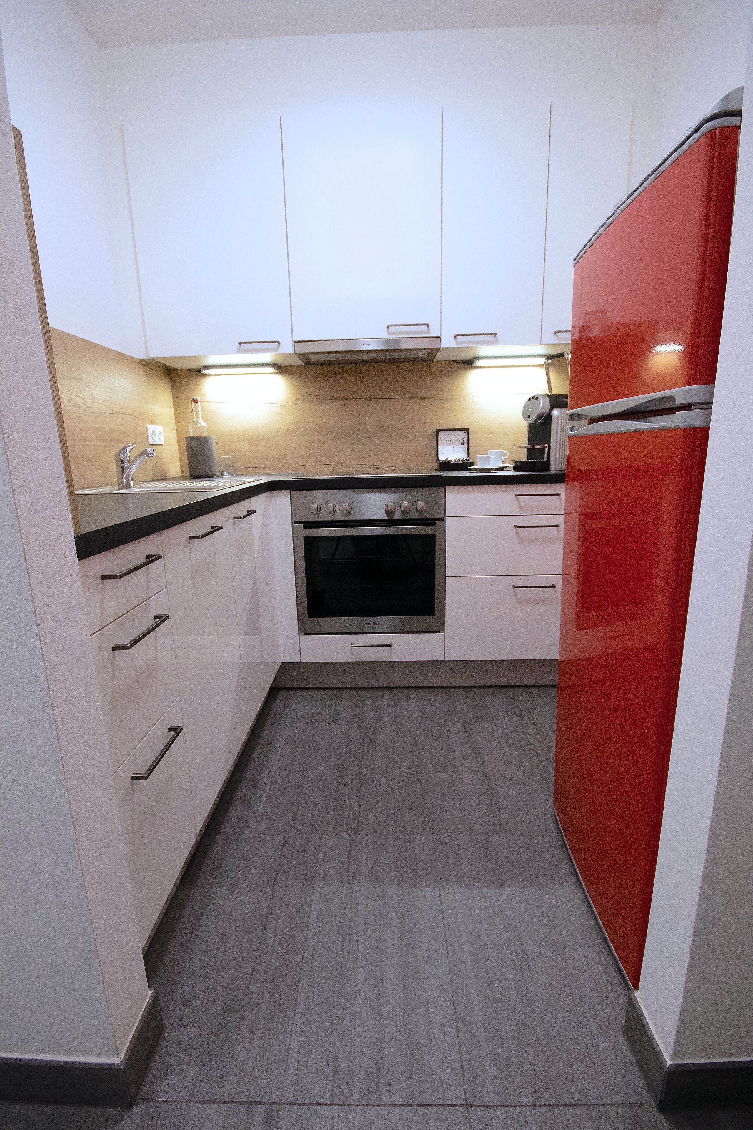 A modern kitchen with white cabinets, a red refrigerator, and a built-in oven.