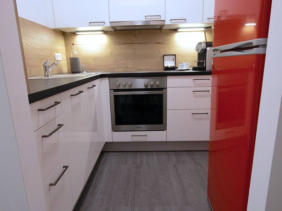A modern kitchen with white cabinets, a red refrigerator, and a built-in oven.