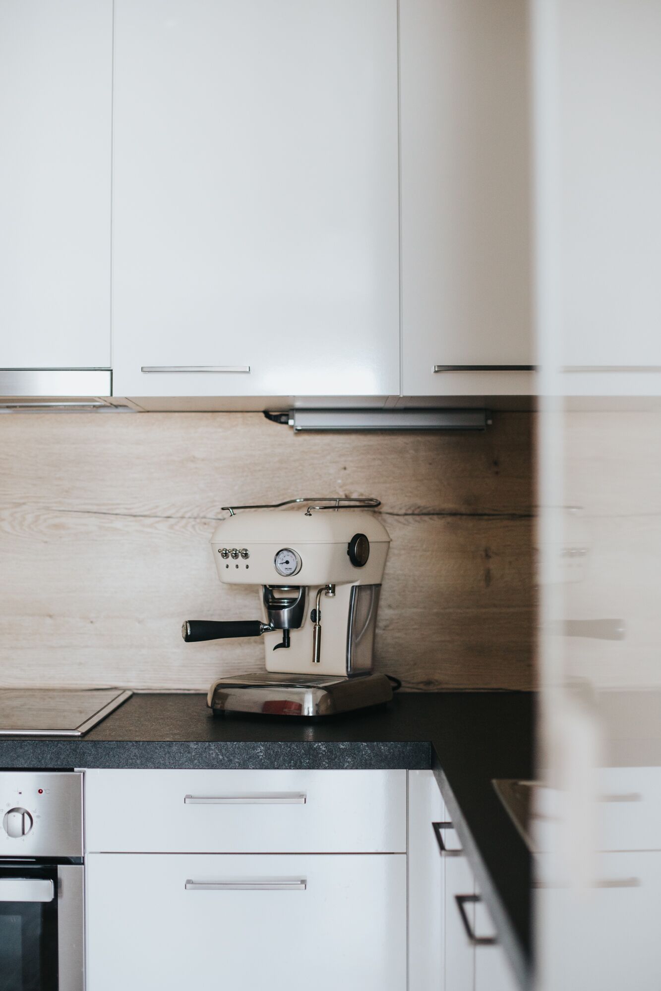 A kitchen with white cabinets, a coffee machine, and a wooden backsplash.