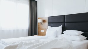 Cama bem arrumada com lençóis brancos, cabeceira escura e luminária fixada na parede.