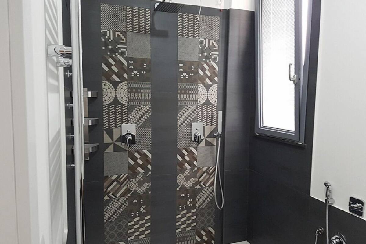 Une salle de bain avec une douche, des carreaux décorés et une fenêtre.