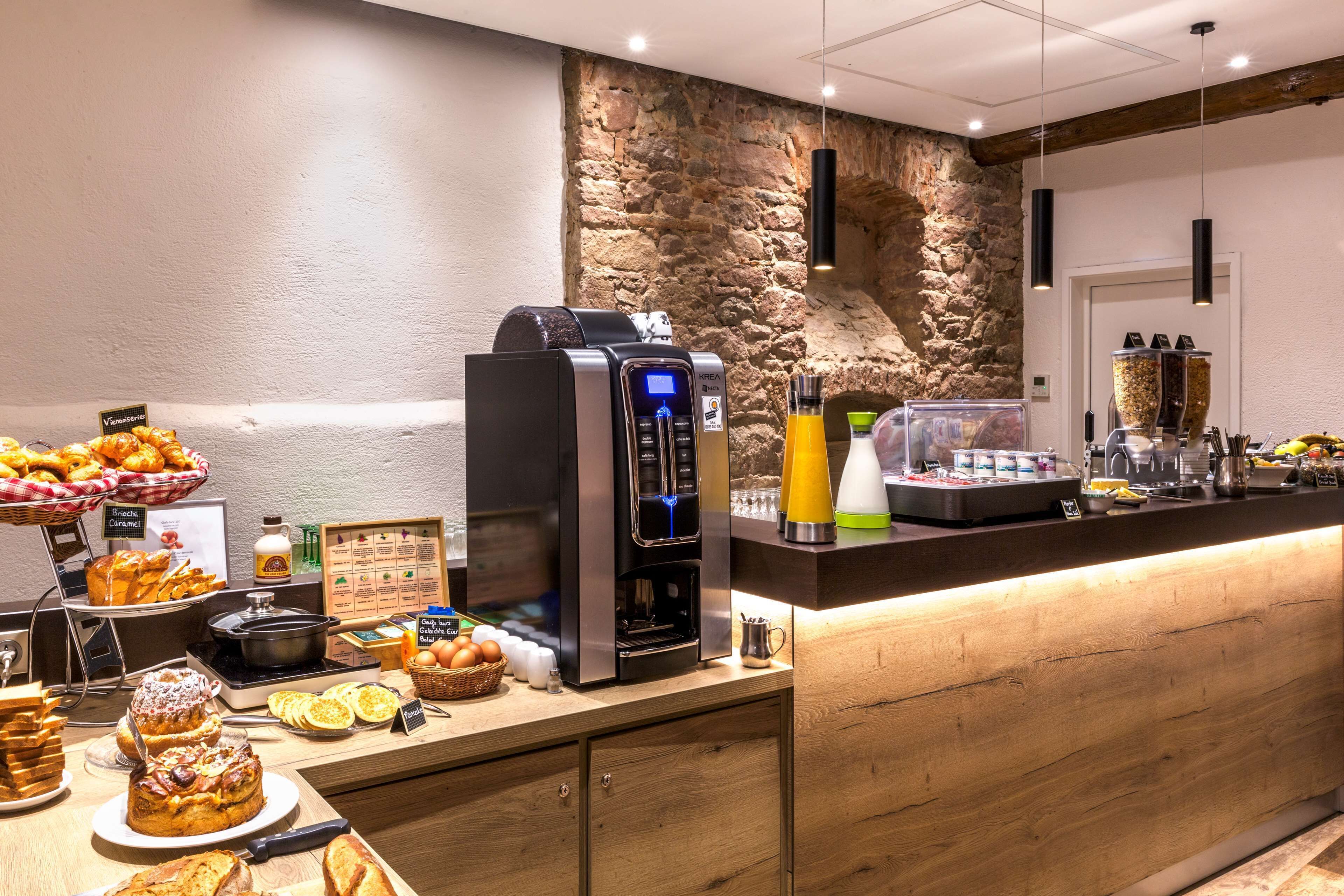 Un buffet de petit-déjeuner avec une machine à café, des fruits, des viennoiseries et un mur en pierre.