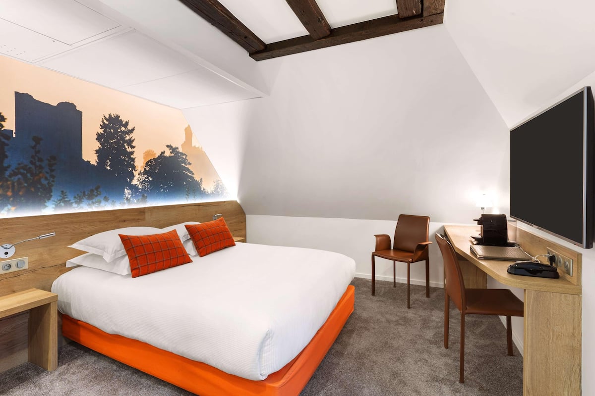 Habitación de hotel con cama, escritorio, silla y televisor grande.