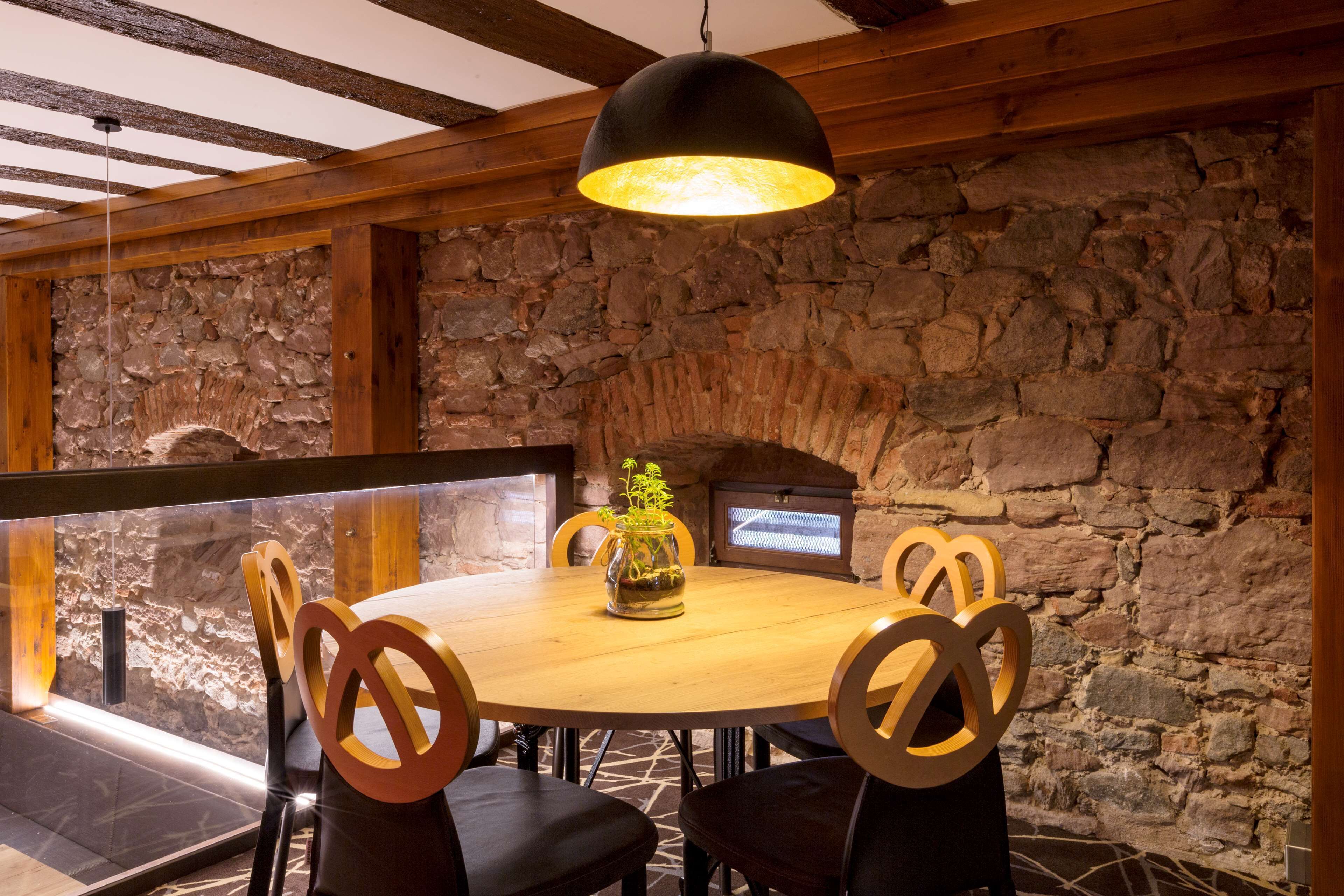 Una mesa redonda de madera con cuatro sillas, una lámpara colgante y una pared de piedra con chimenea.