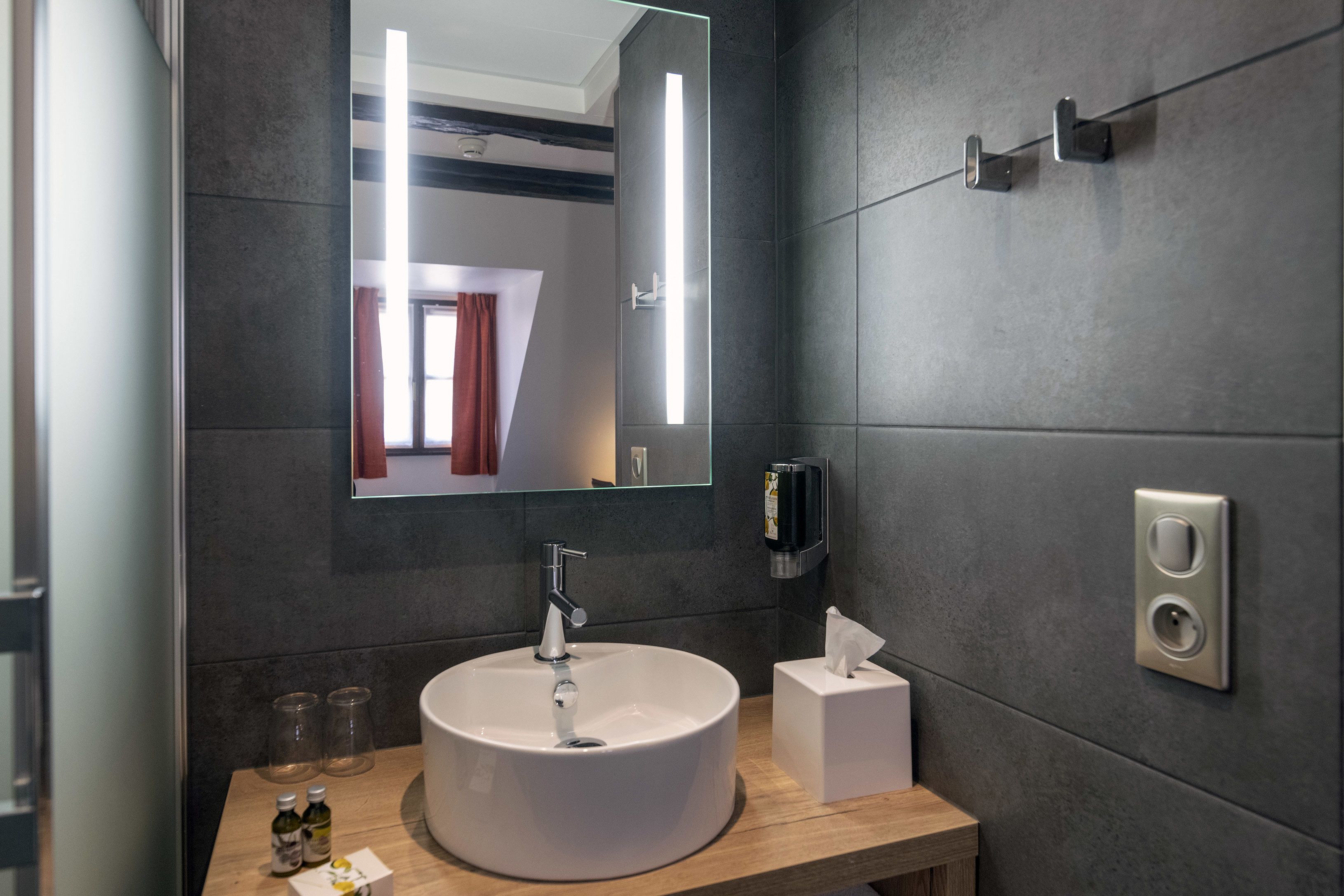 A modern bathroom with a round white sink, a mirror, a towel dispenser, and a tissue box.