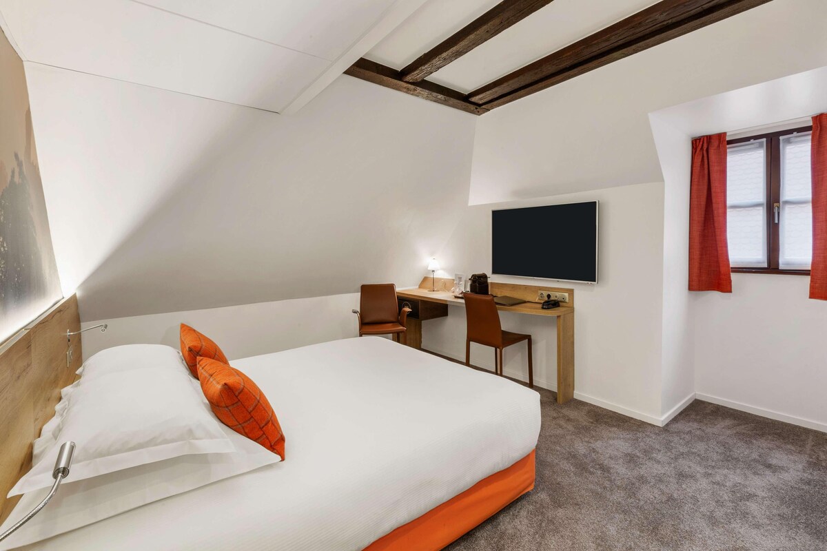 A hotel room with a bed, desk, chair, TV, and window with curtains.