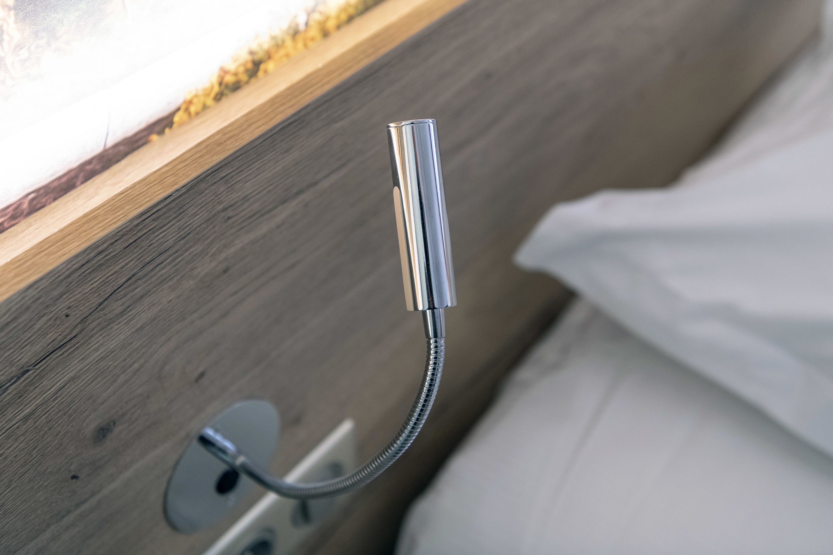 A showerhead mounted on a wooden wall with a white curtain partially visible.