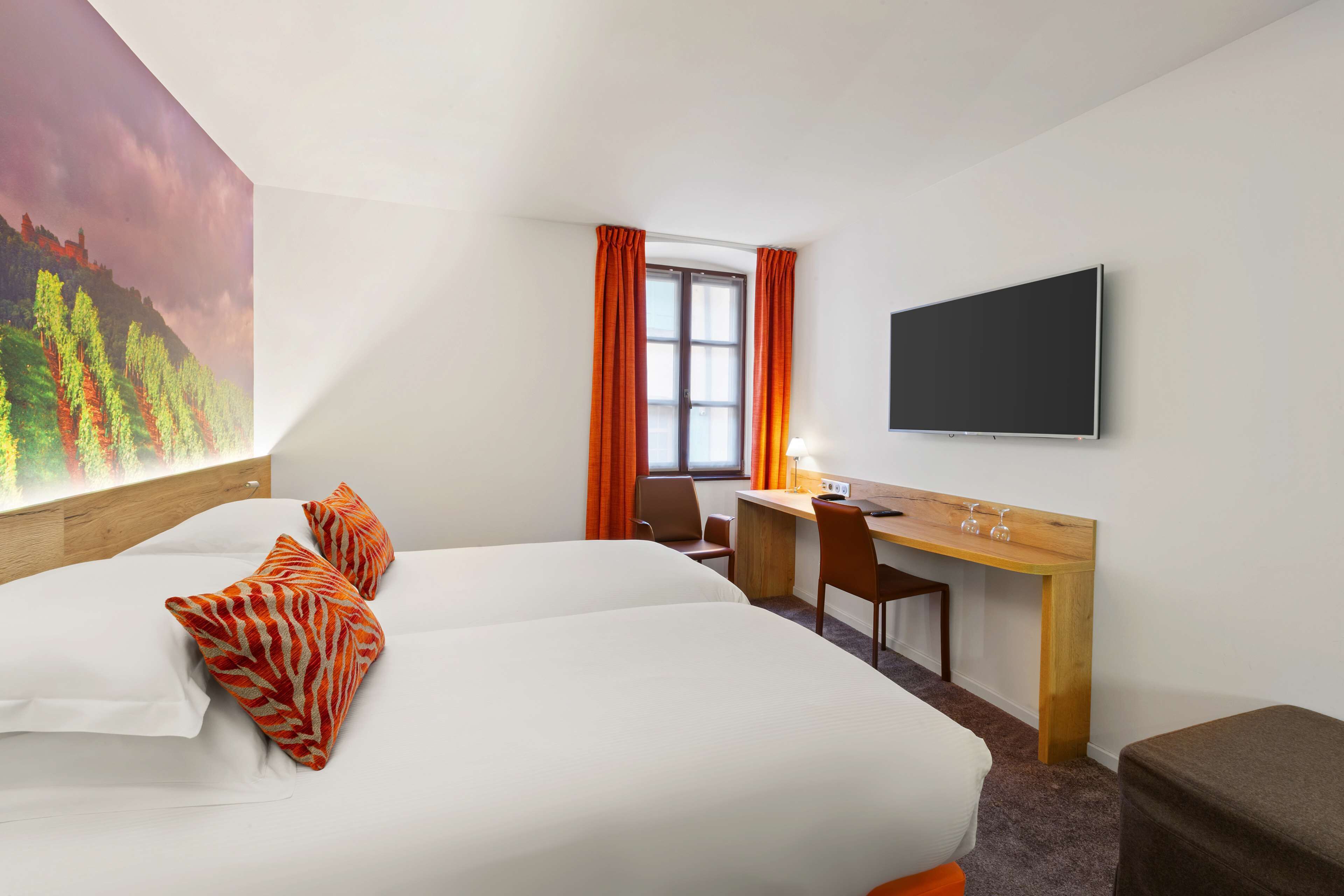 A hotel room with two beds, a desk, a chair, a TV, and a window with curtains.