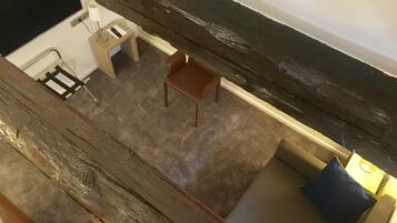 Una habitación con piso de madera, una pequeña mesa con una silla, un sofá y una lámpara.
