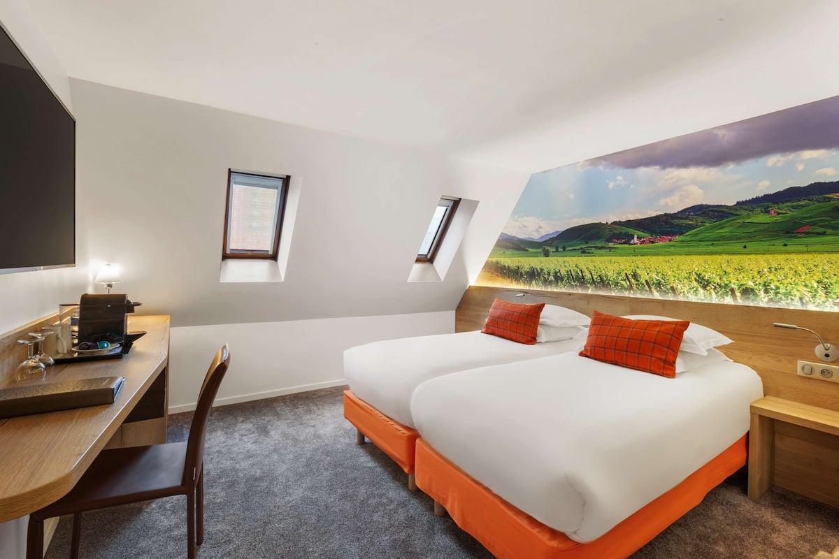 Habitación de hotel con una cama grande, un escritorio, una silla y vistas a un paisaje verde a través de una ventana.