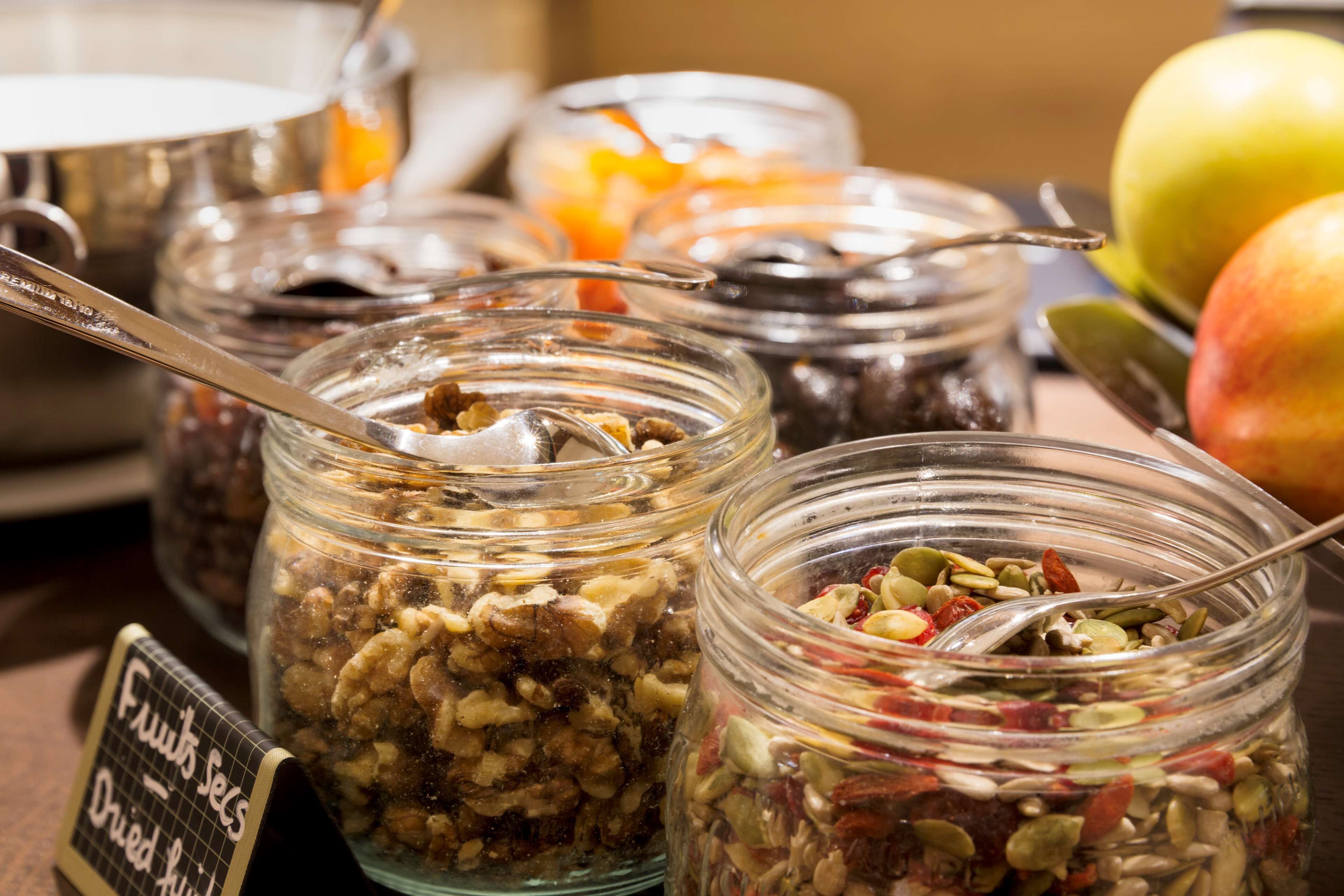 A variety of food items in glass jars, including nuts and dried fruits, with a sign indicating 'Fruits & Nuts - Dried Fruits'.