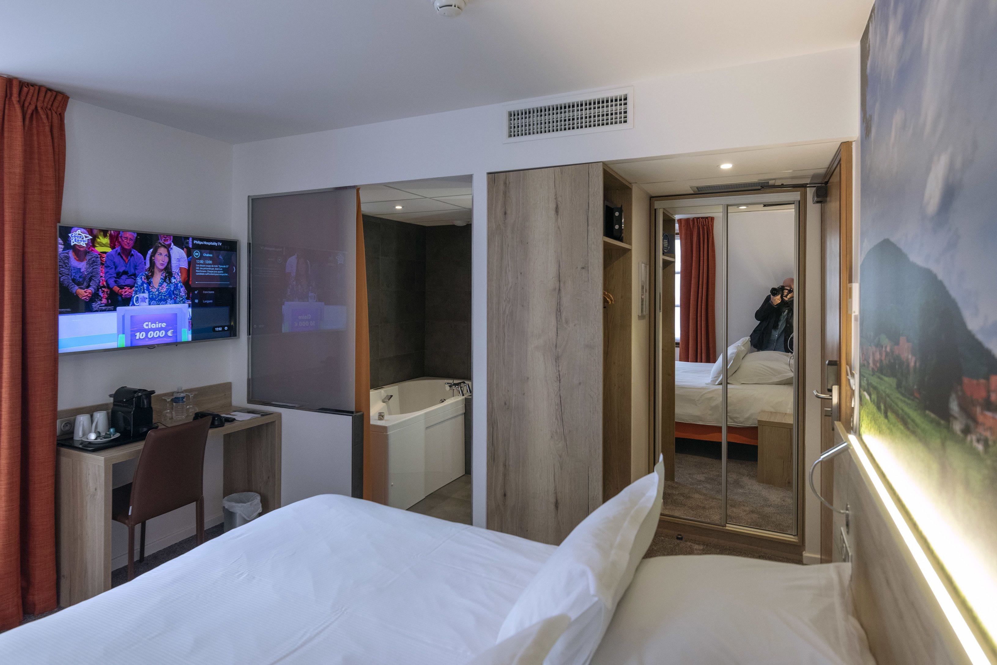 A hotel room with a bed, a desk, a TV, a bathroom, and a large window.