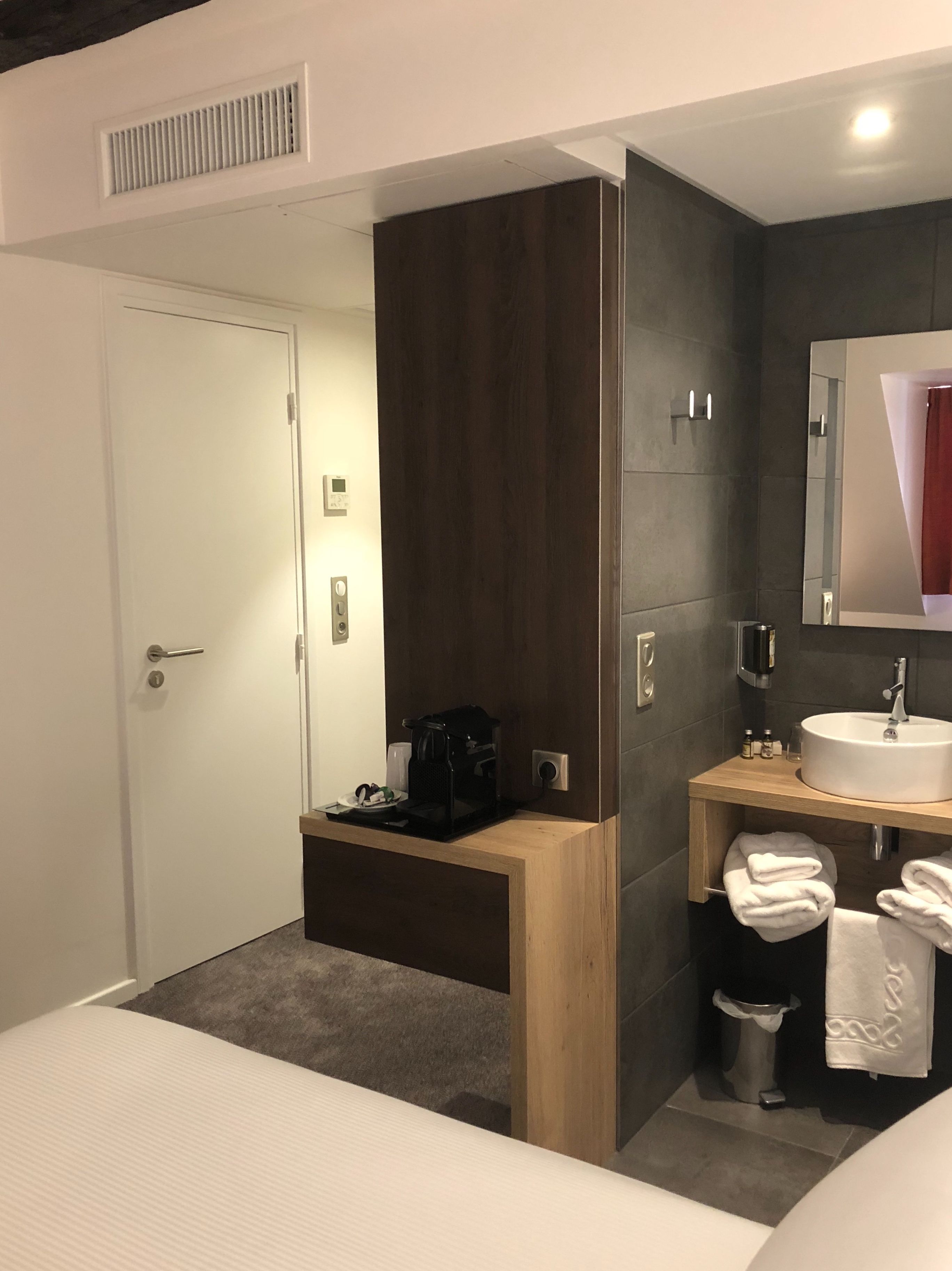 Et moderne hotelværelse med seng, indbygget kaffemaskine, vask og spejl.