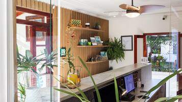 Un área de recepción con un panel de madera en la pared, un ventilador de techo, un mostrador de recepción con una computadora y varias plantas.