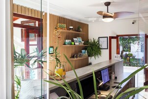 Un área de recepción con un panel de madera en la pared, un ventilador de techo, un mostrador de recepción con una computadora y varias plantas.