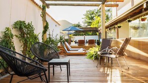 A wooden deck with lounge chairs and umbrellas, surrounded by greenery and a building with large windows. - Pousada Recanto do Jabaquara (Paraty)