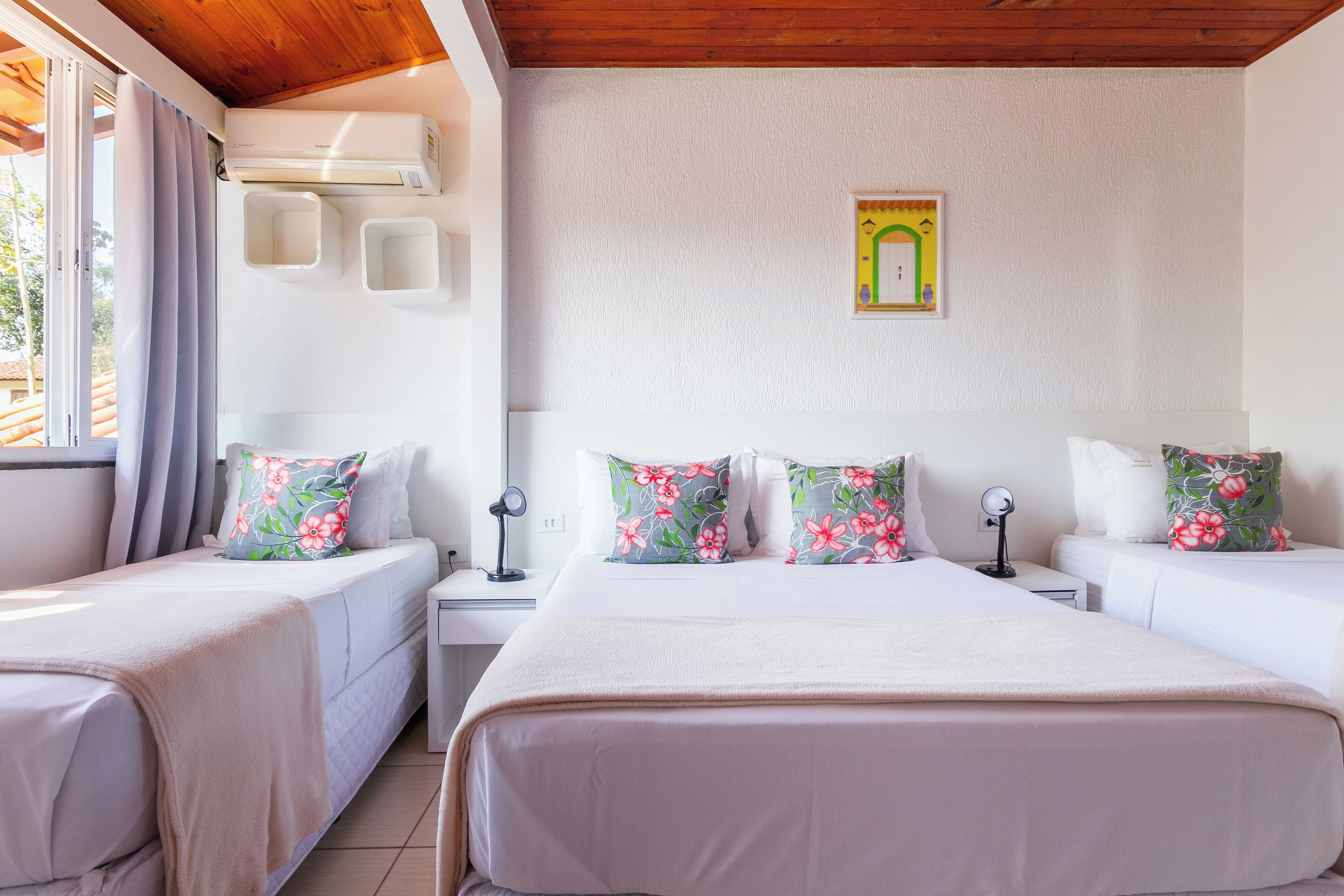 Un dormitorio con dos camas, cada una con almohadas estampadas, un ventilador de techo y un pequeño equipo de aire acondicionado de pared.