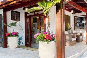 Entrada de hotel com fachada de madeira, grandes vasos com flores coloridas e móveis de vime.