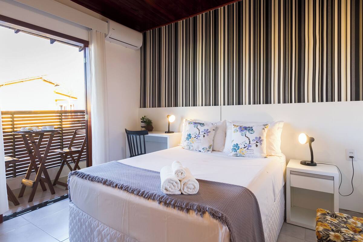 A hotel room with a bed, bedside table, and a view of the outside balcony.