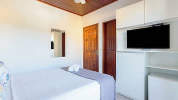 A bedroom with a bed, a television mounted on the wall, wooden doors, and a ceiling fan.
