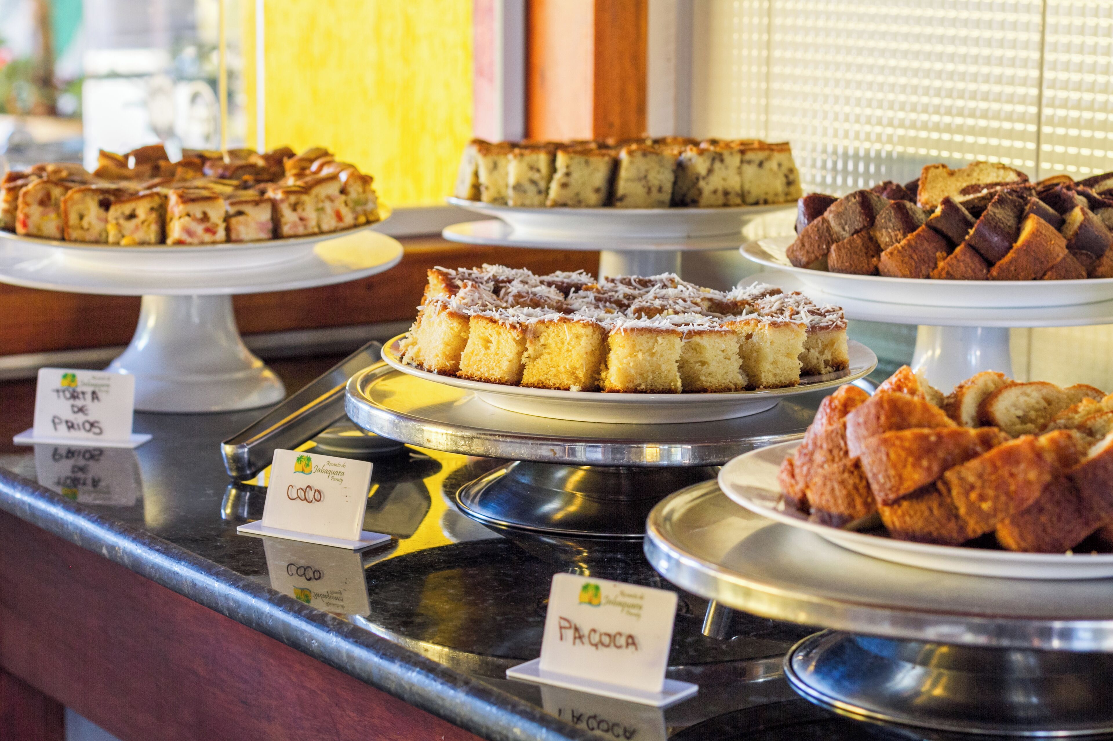 A display of various cakes on a counter with labels indicating names and prices.