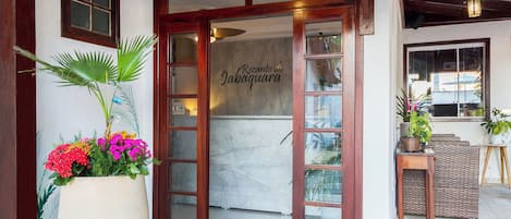 A hotel entrance with a large potted plant, a marble wall, and a wooden door.