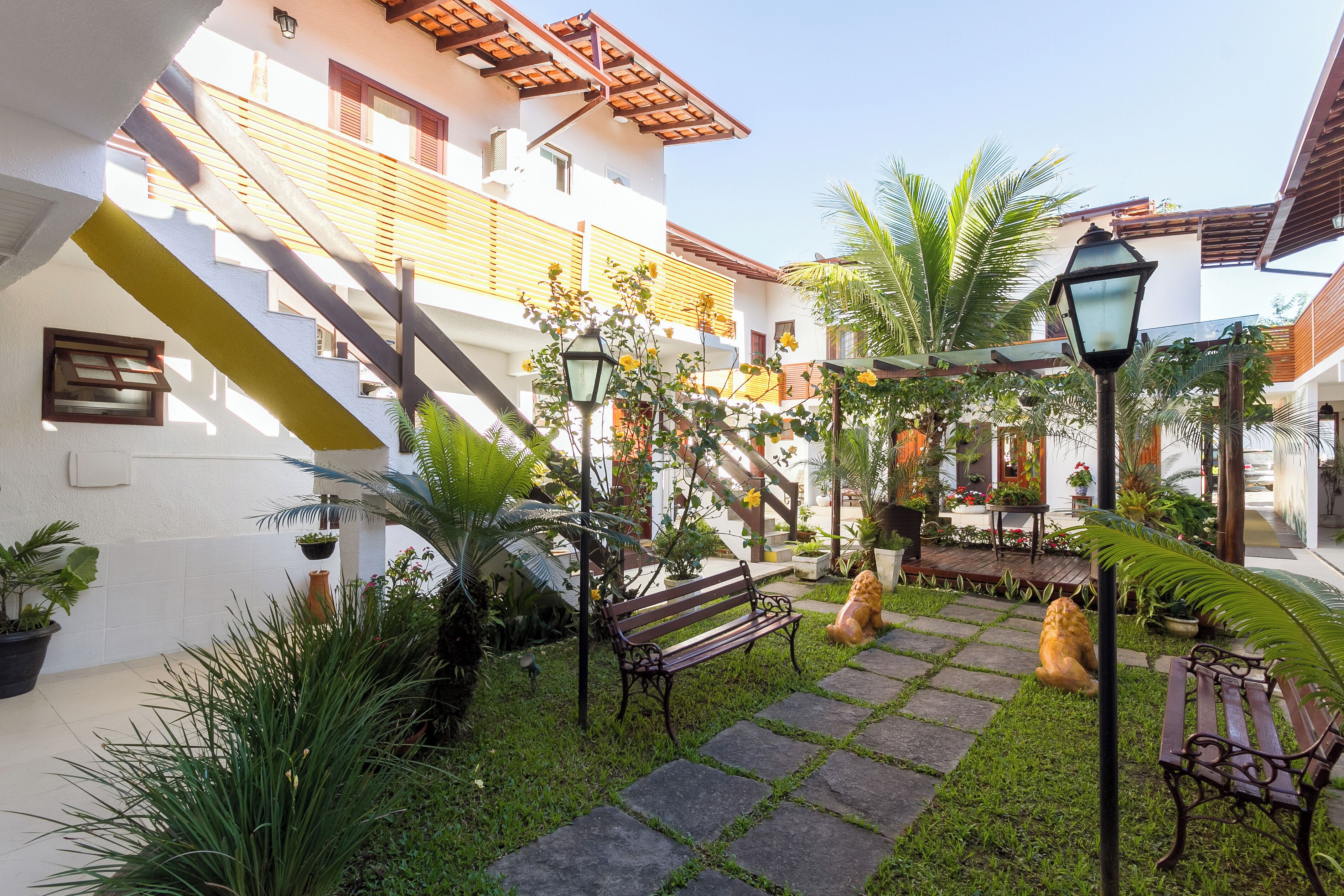 A courtyard with a stone pathway, benches, potted plants, and a staircase.