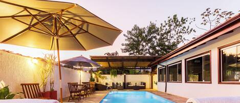 A pool area with lounge chairs, umbrellas, and a covered seating area.