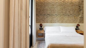 A hotel room with a brick wall, a large bed, two bedside tables with lamps, and a patterned rug. - Colectia Parada del Marqués. (Seville)