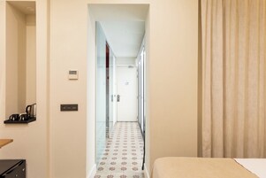 A hotel hallway with a bed, a coffee machine, and a door leading to another room.