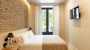 A hotel room with a brick wall, a bed with white linens, a flat-screen TV, and a balcony with curtains. - Colectia Parada del Marqués. (Seville)